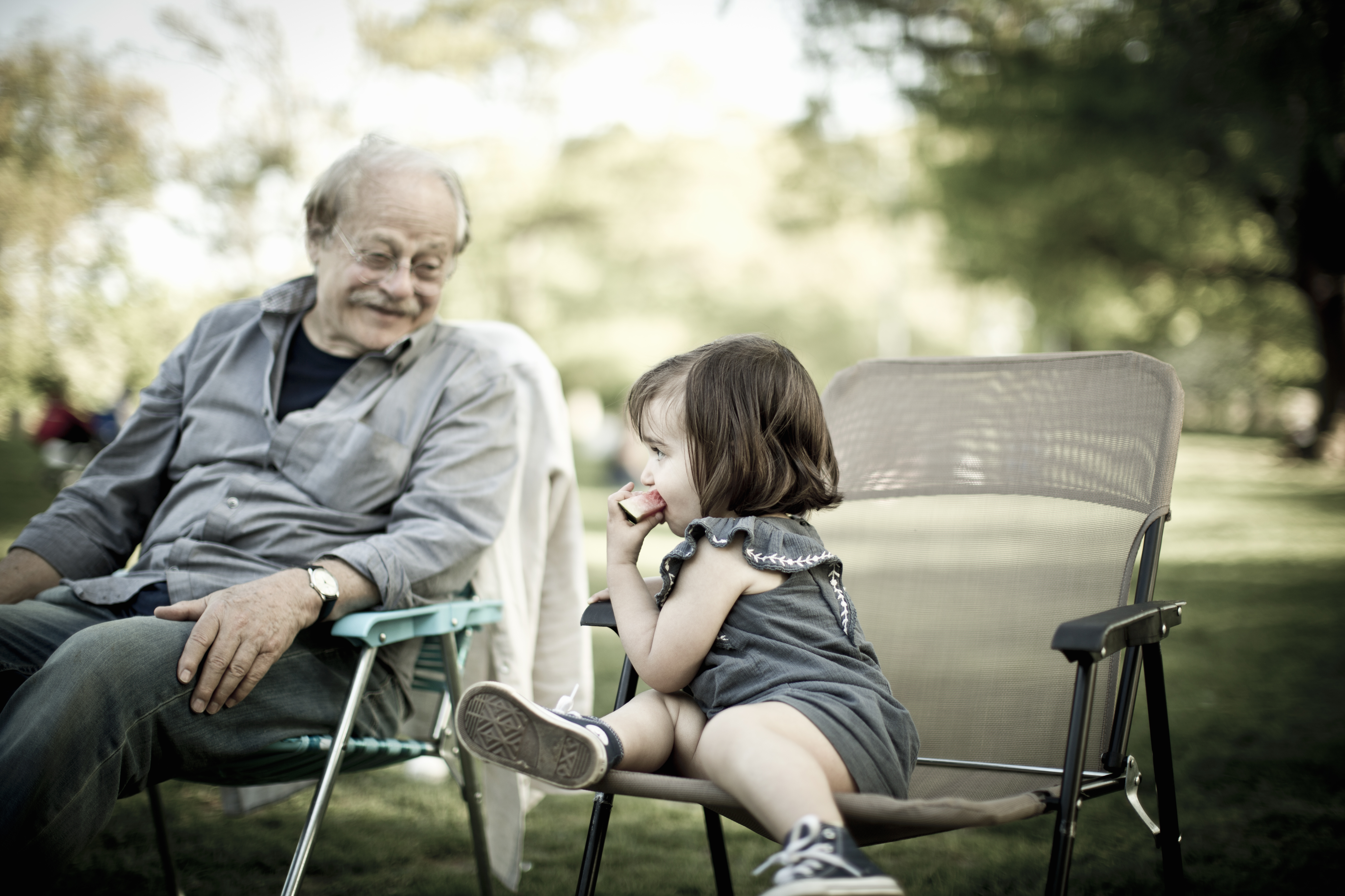 An elderly man sitting with a child at a park.
